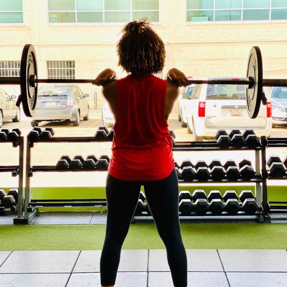 Member pressing a loaded barbell overhead on the Petworth Fitness floor